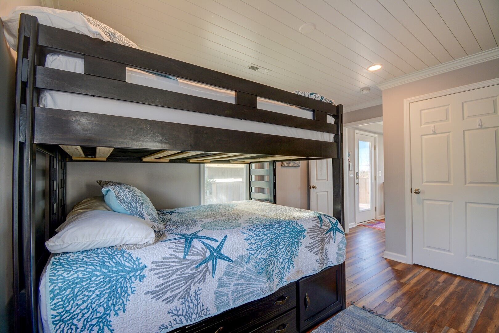 A bunk bed with a patterned bedspread, a nightstand, and a door in the background.
