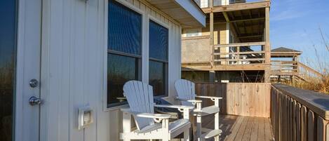 Een houten terras met twee Adirondack-stoelen en een tafel, met uitzicht op een strand.