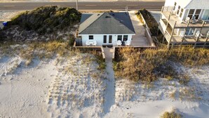 Una casa de playa con terraza de madera, un porche cubierto y vista al océano.