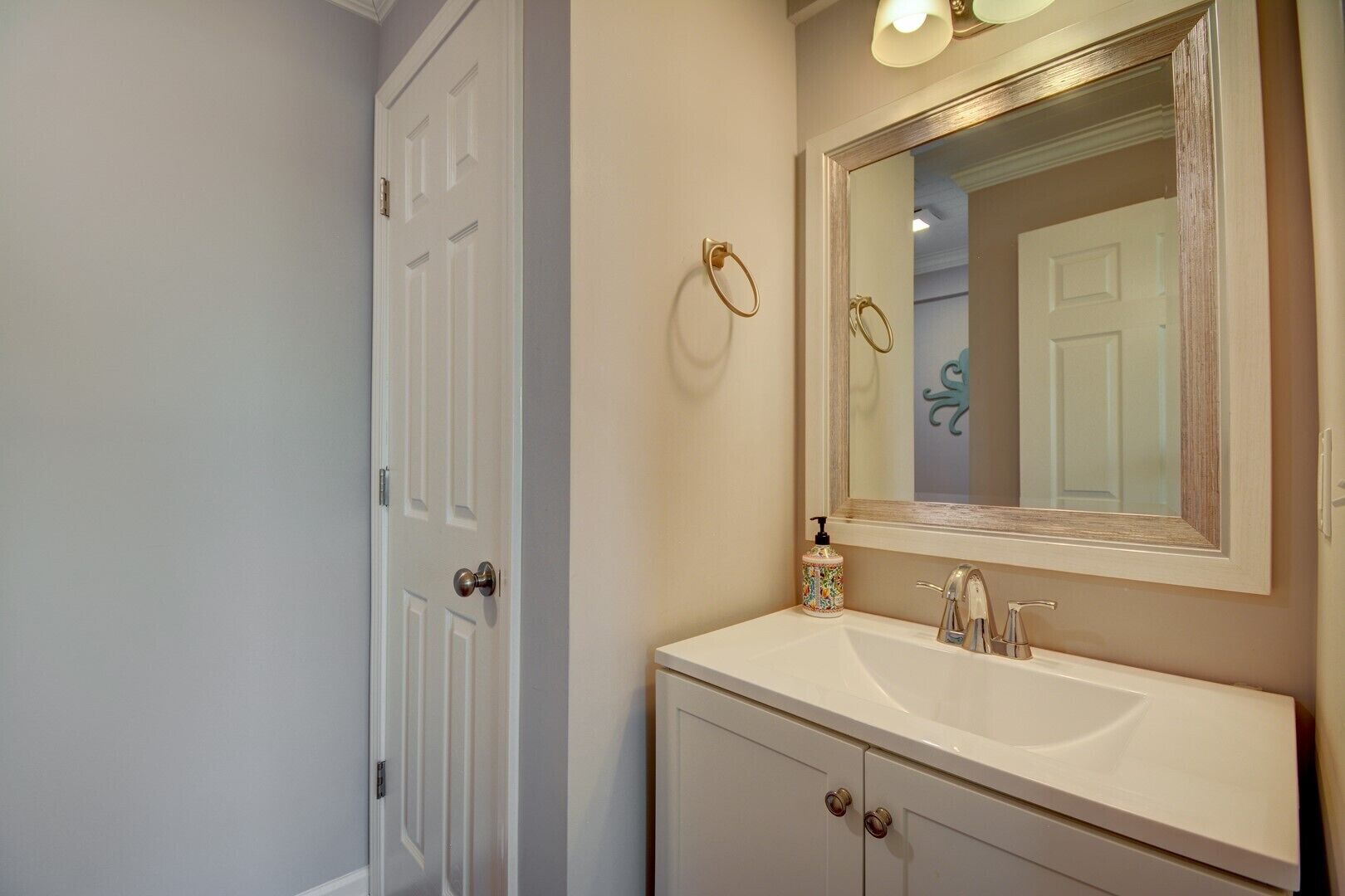 Une salle de bain avec un meuble-lavabo blanc, un grand miroir et une porte dotée d’une poignée de porte ronde.