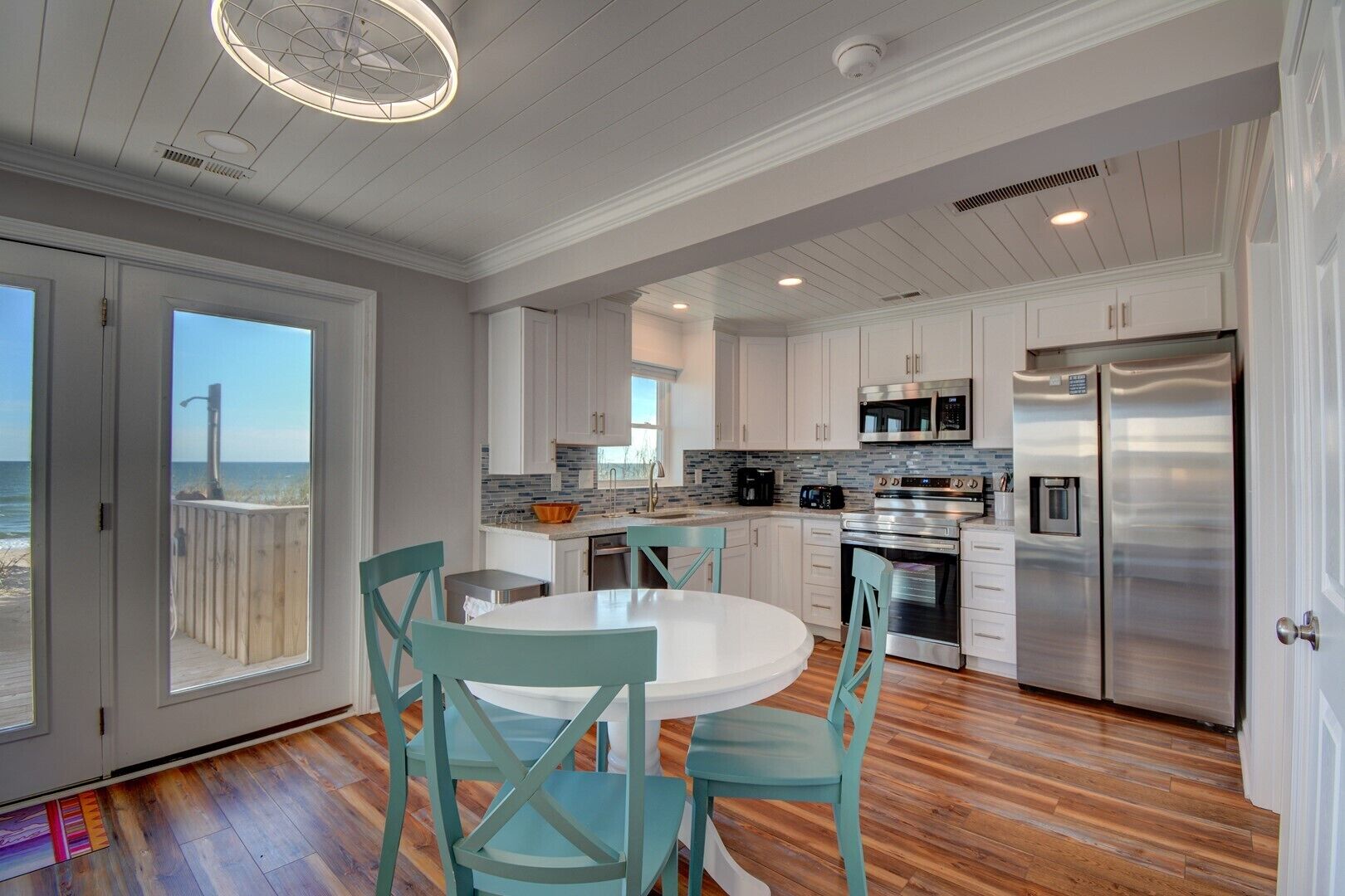 A modern kitchen with white cabinets, stainless steel appliances, and a view to the beach.