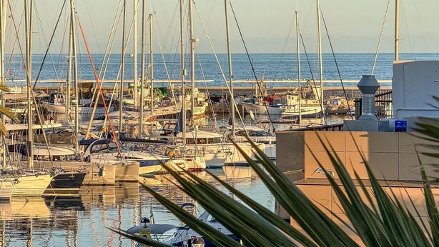 Una marina con diverse imbarcazioni ormeggiate, un molo in pietra e una vista limpida sul mare.