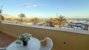 Un balcone con tavolo e sedie, affacciato su una marina con barche e palme.