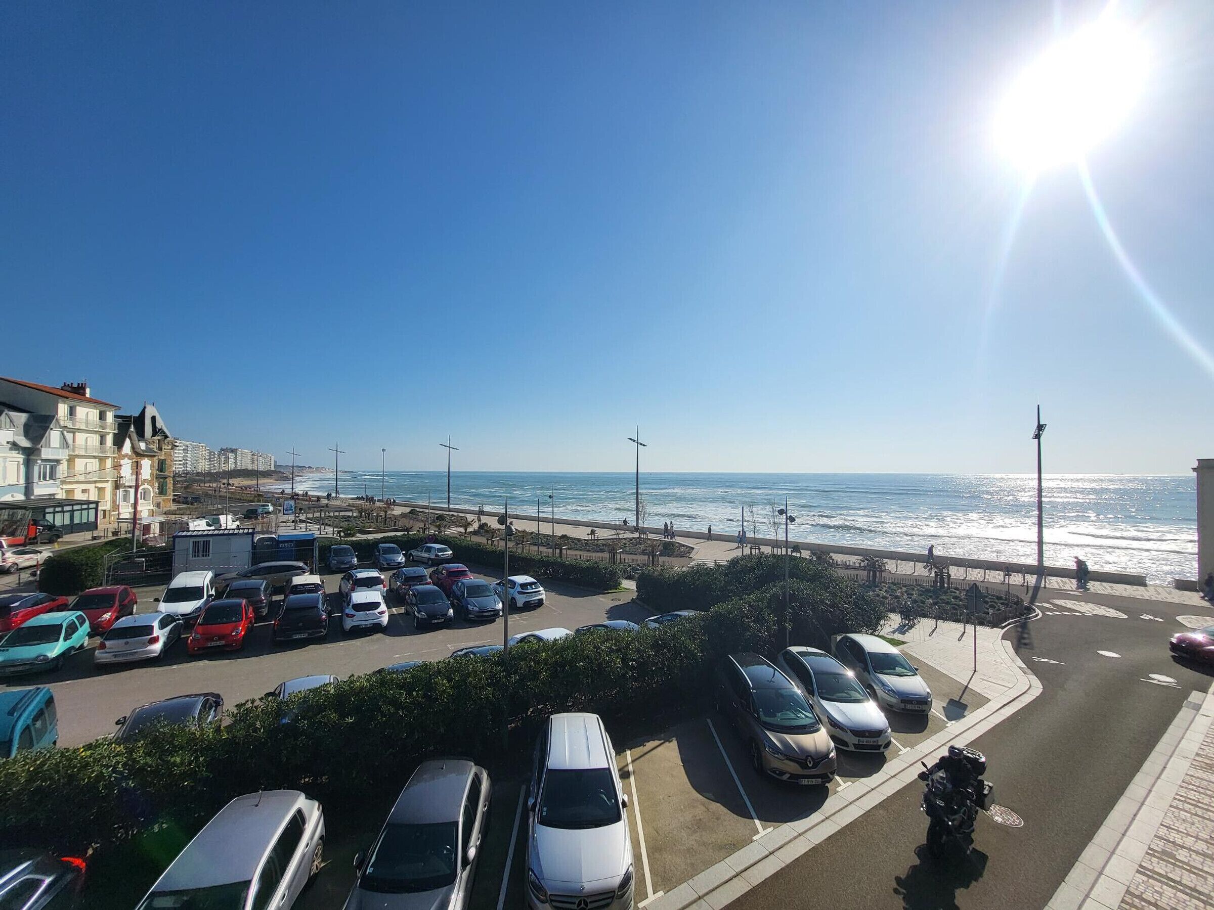 A parking lot with cars and a view of the beach and ocean.
