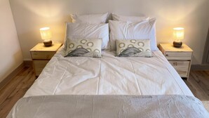 Un lit bien fait, avec une literie blanche et deux coussins décoratifs, flanqué de deux tables de chevet sur lesquelles sont posées des lampes.
