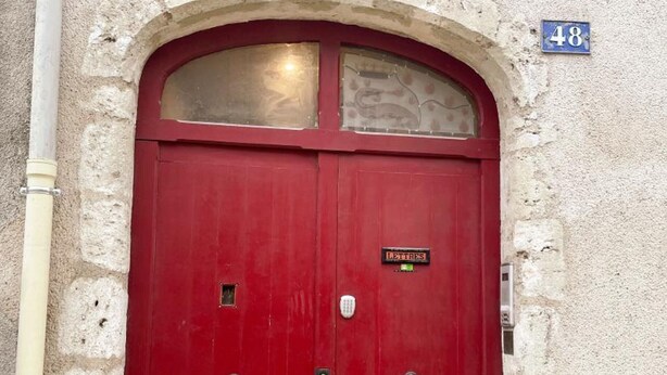 Une porte rouge à deux battants, sur laquelle on peut lire l’inscription « LETTRES », et au-dessus de laquelle figure le numéro de la maison, « 48 ».