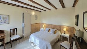 Ein Schlafzimmer mit Holzboden, einem Bett mit weißer Bettwäsche, zwei Nachttischen mit Lampen, einem Sessel und einem kleinen Tisch.