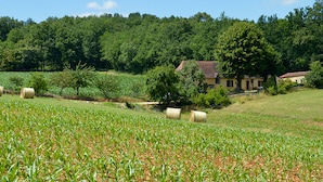 Ländliche Landschaft mit einem Feld, Heuballen und einem von Bäumen umgebenen Haus.