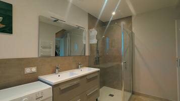 Un bagno moderno con cabina doccia in vetro, mobile doppio lavabo e lavatrice a incasso.
