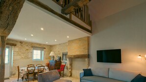A cozy living room with a stone wall, a wooden staircase, a sofa, a glass coffee table, and a dining area with a table and chairs. - Charming lodge with parking, pets allowed, near Château de Clavières (Ardentes)