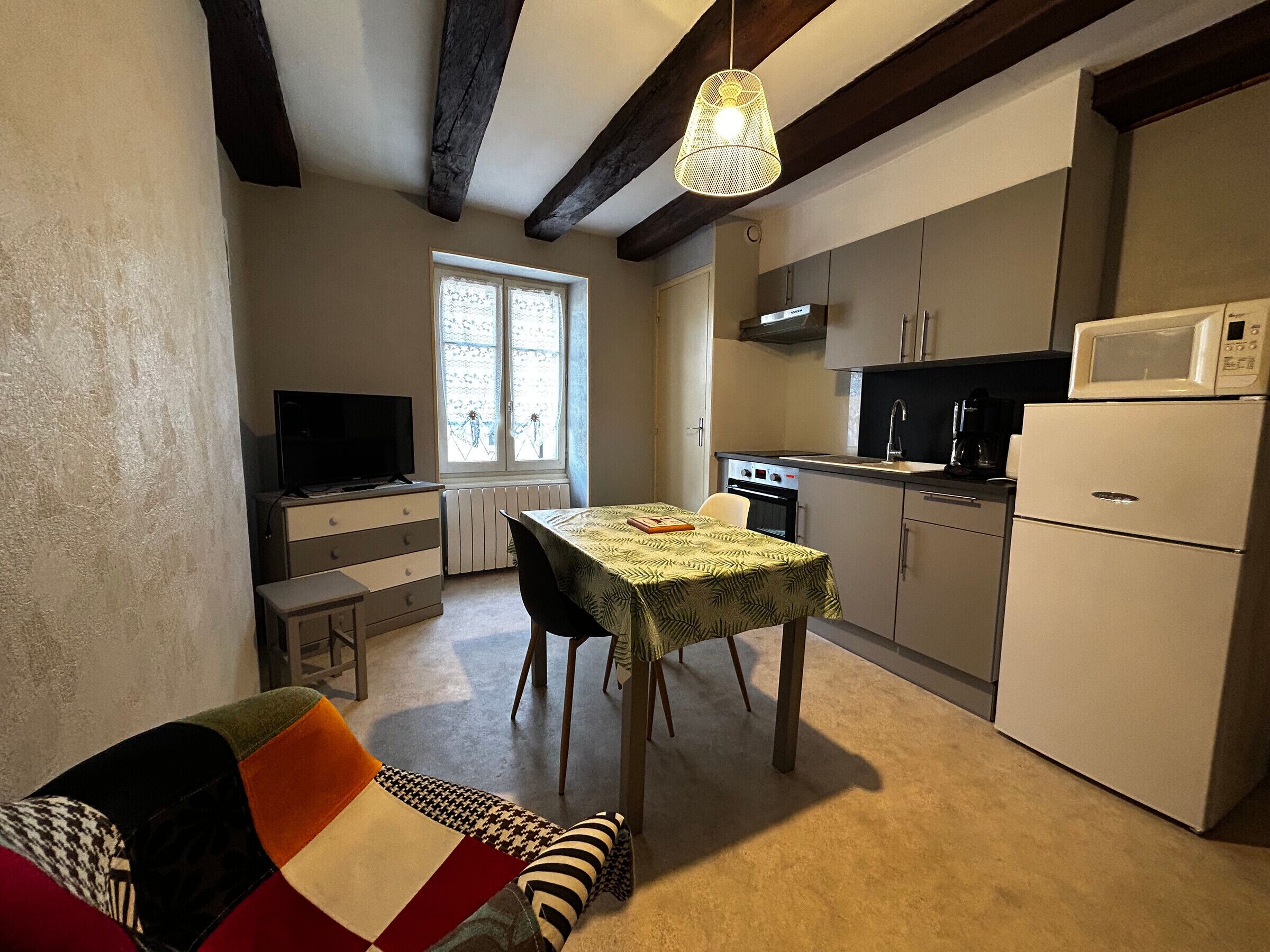 A compact kitchen with a dining area, a television, and a window providing natural light.