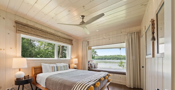 Ein Schlafzimmer mit einem großen Bett, zwei Nachttischlampen, einem Deckenventilator und einem Fenster mit Seeblick.