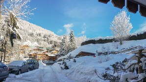 Eine verschneite Straße führt zu einem Berghotel mit mehreren Gebäuden, geparkten Autos und schneebedeckten Bäumen.