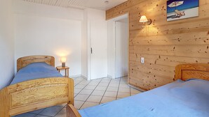 A room with two wooden beds, a wooden wall with a painting, and a tiled floor.