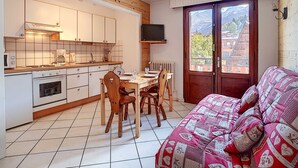 A cozy kitchen with wooden cabinets, a dining table with chairs, and a sofa with a patterned cover.