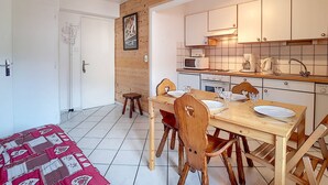 A compact kitchen with white cabinets, a wooden dining table, and a small stool.