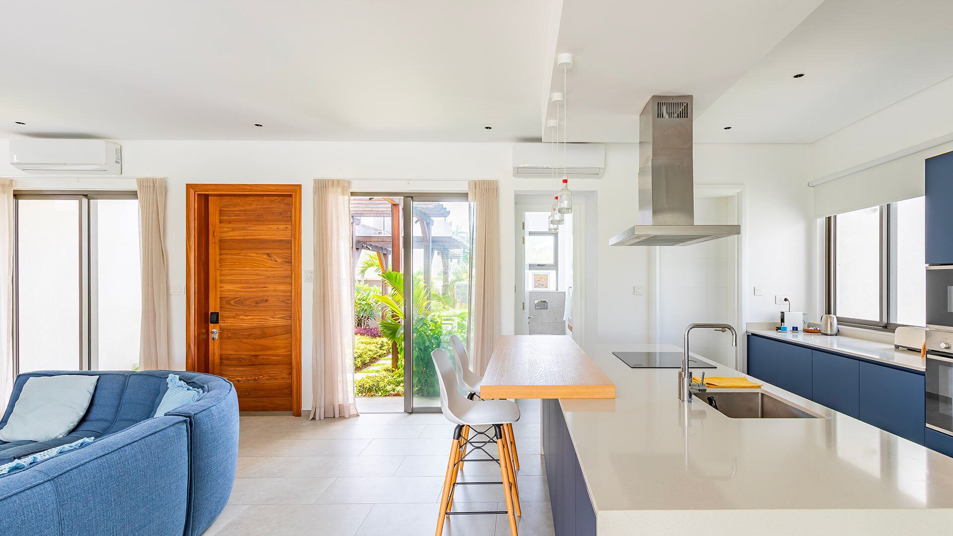 Een moderne keuken met een centraal eiland, een eetgedeelte met een houten tafel en een woonkamer met een blauwe bank.