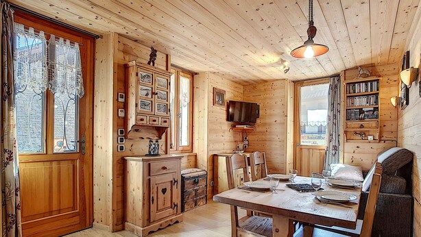 Un interior de madera con una mesa de comedor, sillas, un televisor y una estantería.
