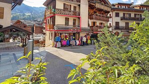 Un edificio de estilo chalé tradicional con balcones, un local comercial en la planta baja y un paisaje montañoso de fondo.