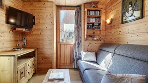 Interior acogedor de una cabaña con detalles de madera, un sofá, una mesita, una estantería y un televisor.