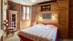 Un dormitorio de cabaña de madera con cama, una silla, un tocador y una ventana.