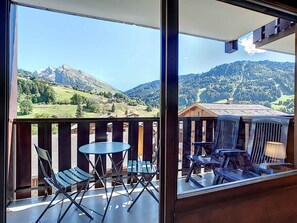 En balkon med udsigt over et bjergrigt landskab, et trægelænder og et bord med stole.