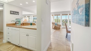 A modern kitchen with white cabinets, a coffee machine, and a sink. There is a balcony with a view of the outside.