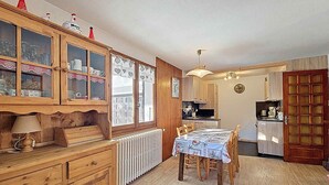 Ett mysigt kök med träskåp, ett matbord med stolar och ett kylskåp.