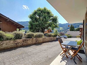 A patio with a table and chairs, a stone wall, and a view of a tree and mountains in the background. - 4-person apartment in La Clusaz with terrace and pets allowed (La Clusaz)
