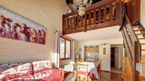 A cozy living room with a red sofa, wooden dining table, and a staircase leading to an upper level. - Cozy Duplex in La Clusaz - 6 pax, pets allowed (La Clusaz)