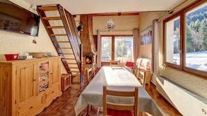 A cozy dining area with a wooden table, chairs, and a fireplace. A wooden cabinet and a television are also visible. - Cozy Duplex in La Clusaz - 6 pax, pets allowed (La Clusaz)