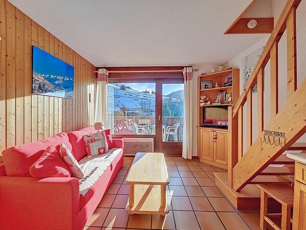 Un salón acogedor con un sofá rojo, paredes de madera, vistas a montañas y una escalera de madera.