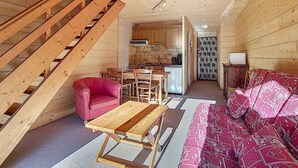 A cozy cabin interior with a wooden staircase, a dining area with a table and chairs, a kitchen with cabinets and appliances, and a patterned sofa. - Cozy Duplex 4 pers, La Clusaz, pets allowed (La Clusaz)