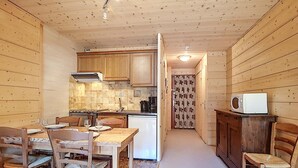 A compact kitchen with wooden cabinets, a dining table with chairs, and a microwave on a cabinet. - Cozy Duplex 4 pers, La Clusaz, pets allowed (La Clusaz)