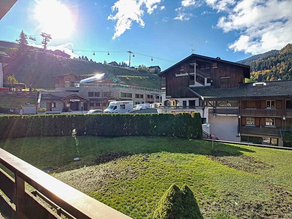 A mountain resort with a ski lift, a wooden building labeled "CRET DU MERLE," and a parking area.