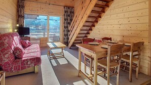 A cozy cabin interior with a wooden staircase, a sofa, a dining table with chairs, and a television. - Cozy Duplex 4 pers, La Clusaz, pets allowed (La Clusaz)
