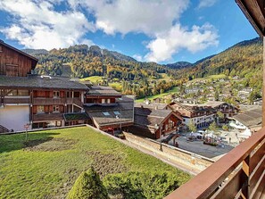 Il s’agit d’un bâtiment traditionnel en bois, doté d’un balcon, d’un petit espace de stationnement et offrant une vue sur un paysage montagneux avec un village en contrebas.