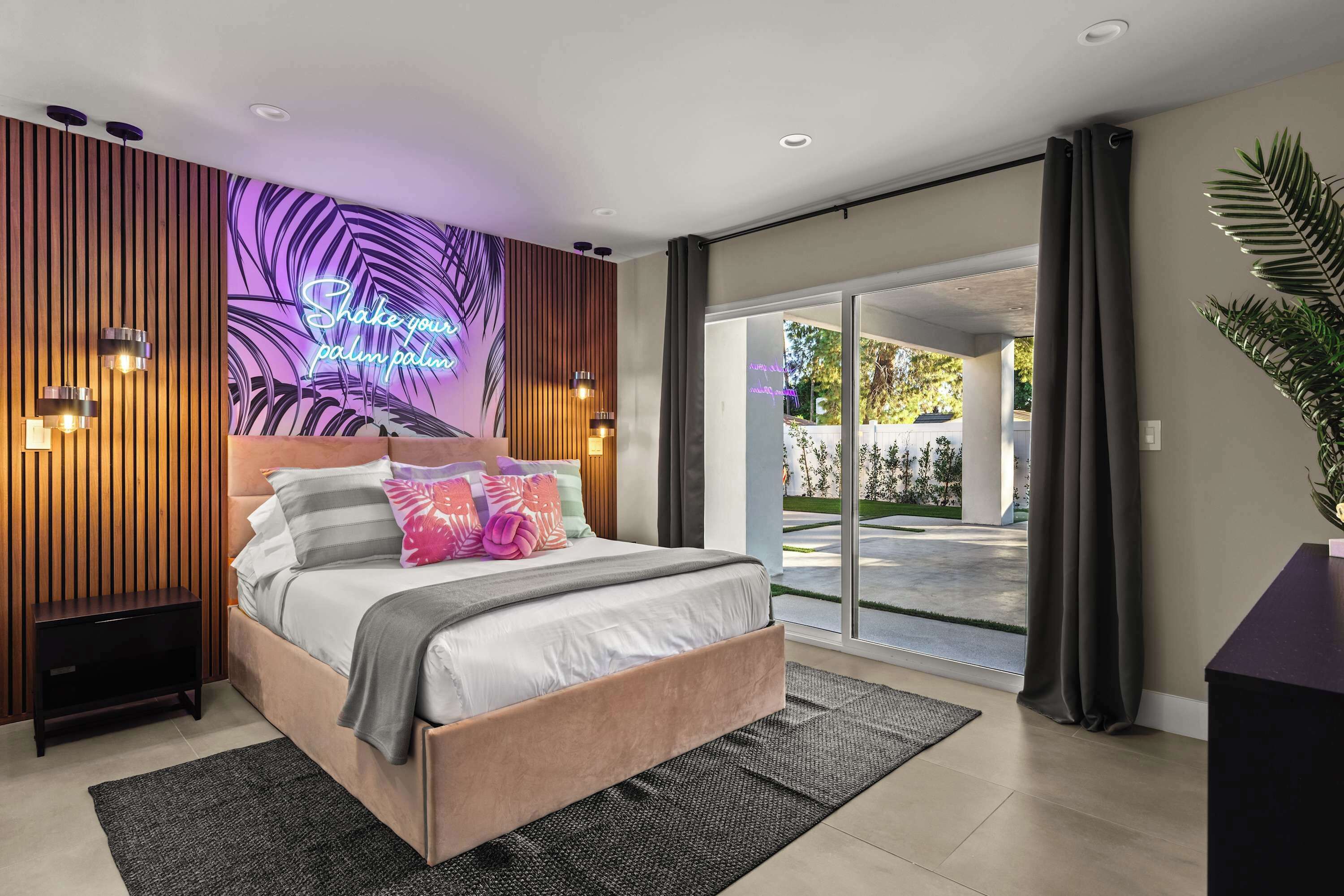 Une chambre à coucher moderne avec un lit, un néon, une grande fenêtre et une vue sur l’extérieur.