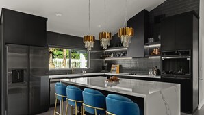 A modern kitchen with a central island, bar stools, and pendant lighting. - THE GLAM PALMS (MountainViews/Sauna/EVCharger/BBQ/Golf/HeatedPool) (Palm Springs)
