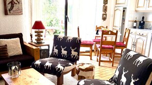 Una sala de estar acogedora con un sofá, sillones, una mesita, una lámpara y una cocina al fondo.