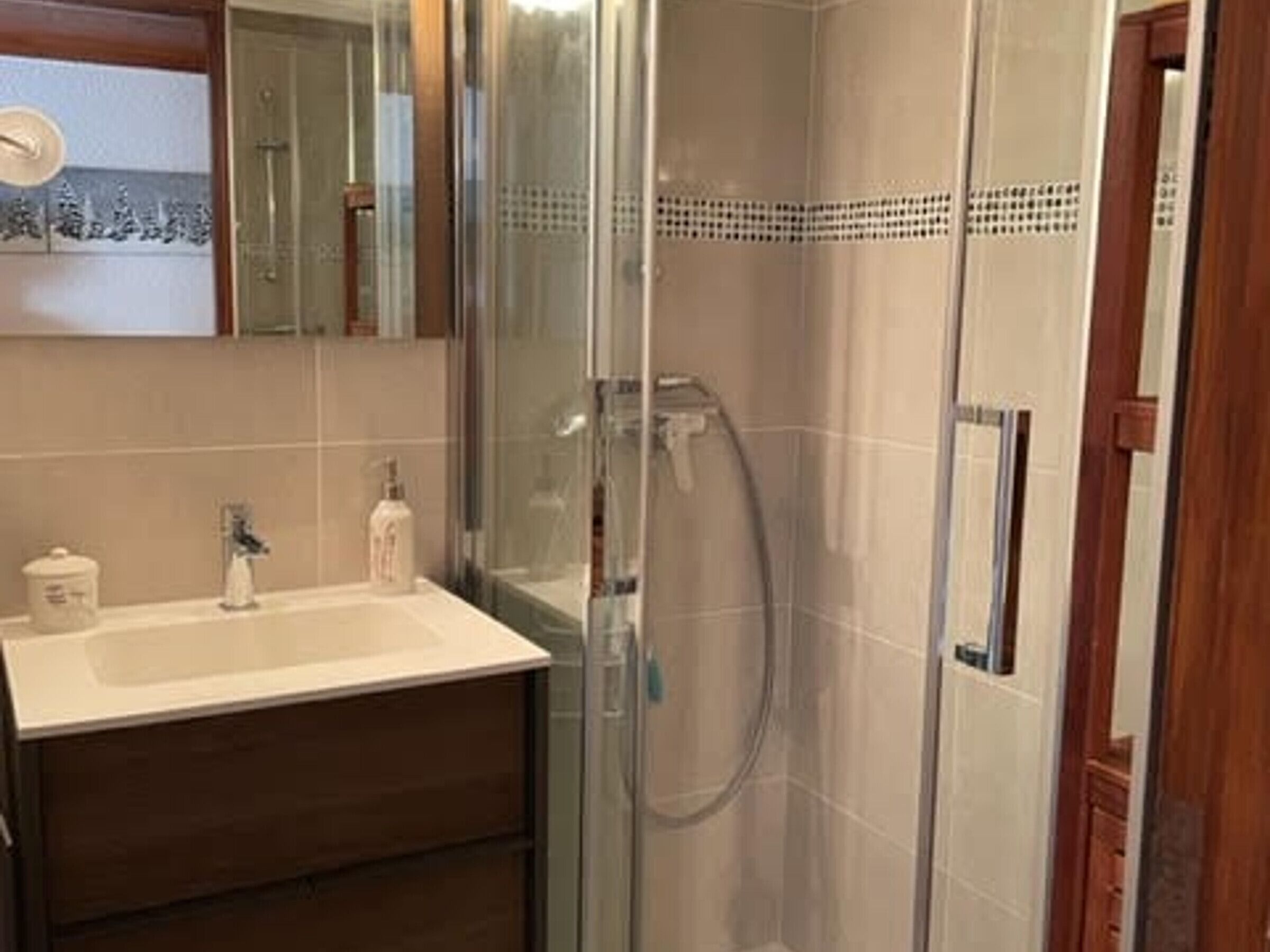 A bathroom with a glass shower enclosure, a sink with a mirror, and a wooden cabinet.