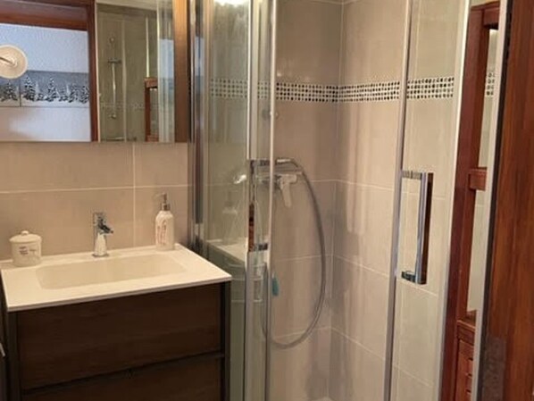 A bathroom with a glass shower enclosure, a sink with a mirror, and a wooden cabinet.