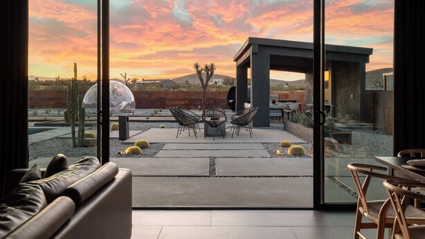 Un intérieur moderne avec une grande porte vitrée donnant sur un patio extérieur aménagé avec un espace salon et offrant une vue sur un paysage désertique.