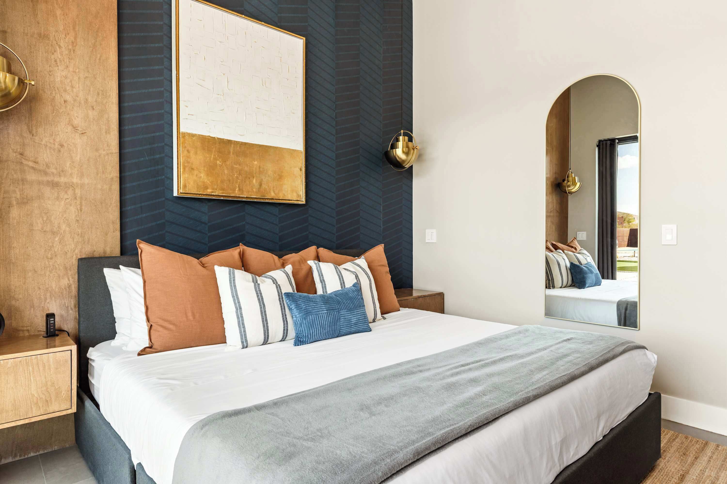 Un dormitorio moderno con una cama grande, una mesita de noche, una lámpara de pared y un espejo.