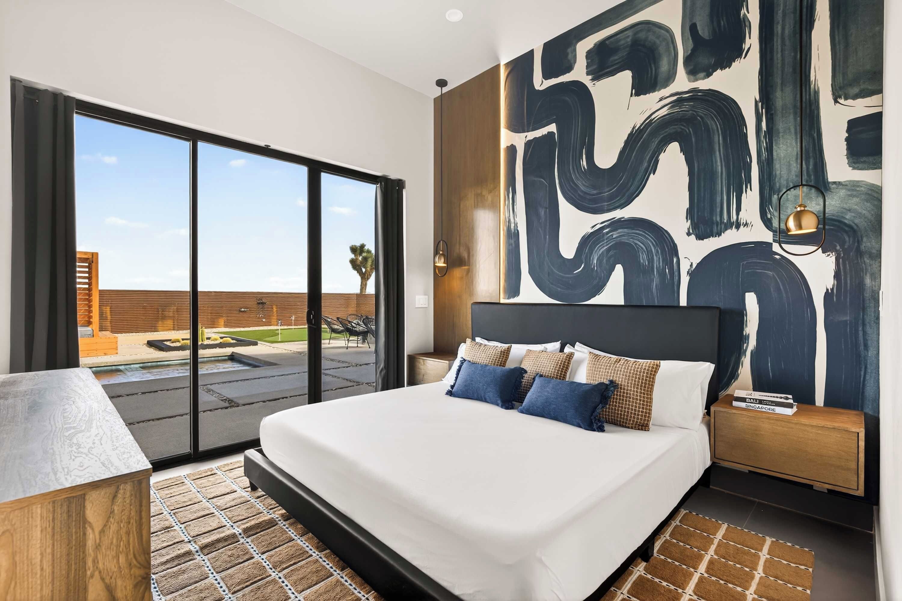 A modern hotel room with a large bed, a view of the outdoors, and a contemporary abstract painting on the wall.