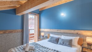 A bedroom with a bed, pillows, a nightstand, and a window with curtains. - Luxury ski-in apartment, sleeps 8, Wi-Fi (Huez)