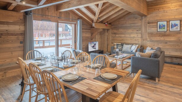 A wooden interior with a dining table set for six, a sofa, and a television in a room with wooden walls and a sloped ceiling. - Luxury ski-in apartment, sleeps 8, Wi-Fi (Huez)