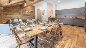 A modern kitchen with grey cabinets, a wooden dining table set for six, and a cozy seating area with a sofa and chairs. - Luxury ski-in apartment, sleeps 8, Wi-Fi (Huez)