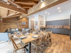 A modern kitchen with grey cabinets, a wooden dining table set for six, and a cozy seating area with a sofa and chairs. - Luxury ski-in apartment, sleeps 8, Wi-Fi (Huez)