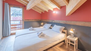 A bedroom with two beds, wooden beams on the ceiling, a window with curtains, and a nightstand with a lamp. - Luxury ski-in apartment, sleeps 8, Wi-Fi (Huez)